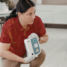 woman holding an automated external defibrillator and explaining how to use it to a group of people
