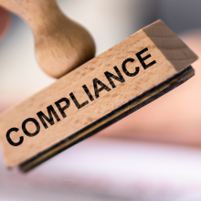 a hand holding a stamp that reads "compliance"