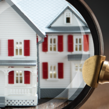 hand holding magnifying glass up to model house on wooden background