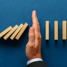 businessman's hand stopping falling dominoes