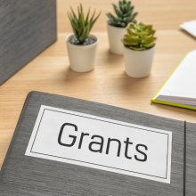 desk surface with papers and a folder labeled "Grants"
