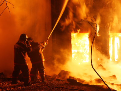 two firefighters spraying water on a burning structure