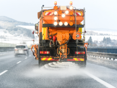 photo of the back of a truck spreading salt on a highway in winter