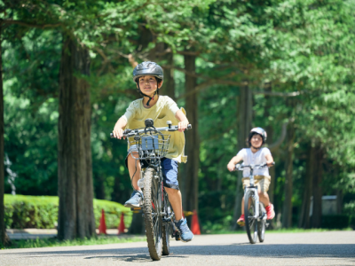 two children riding bicycles on a path lined with trees