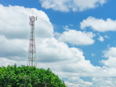 Photo of cell tower taller than trees, against blue sky with fluffy clouds