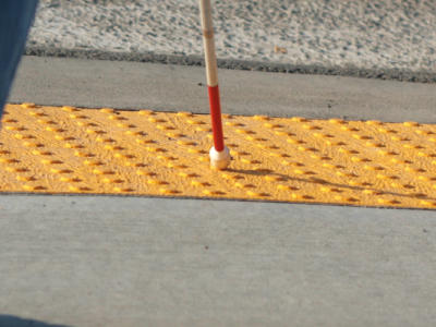 person using a cane crossing the street at a textured curb cut