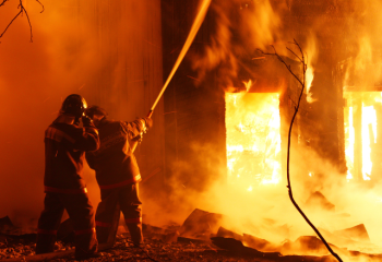 two firefighters spraying water on a burning structure