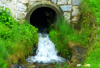 water exiting a stone culvert into an eroded ditch