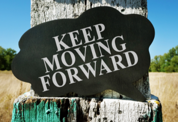 sign reading "Keep Moving Forward" sitting on a tree stump