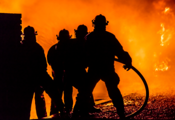 silhouette of four firefighters in front of blaze