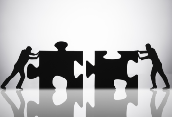 two people fitting large jigsaw puzzle pieces together