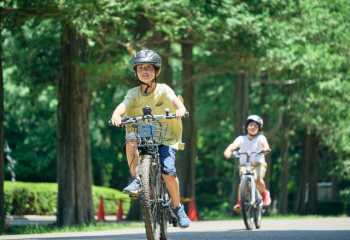 two children riding bicycles on a path lined with trees