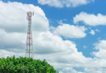 Photo of cell tower taller than trees, against blue sky with fluffy clouds