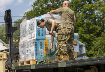 two Vermont National Guard troops unloading pallets of drinking water from a flatbed truck