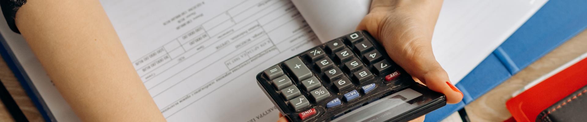 person holding open book and calculator at computer