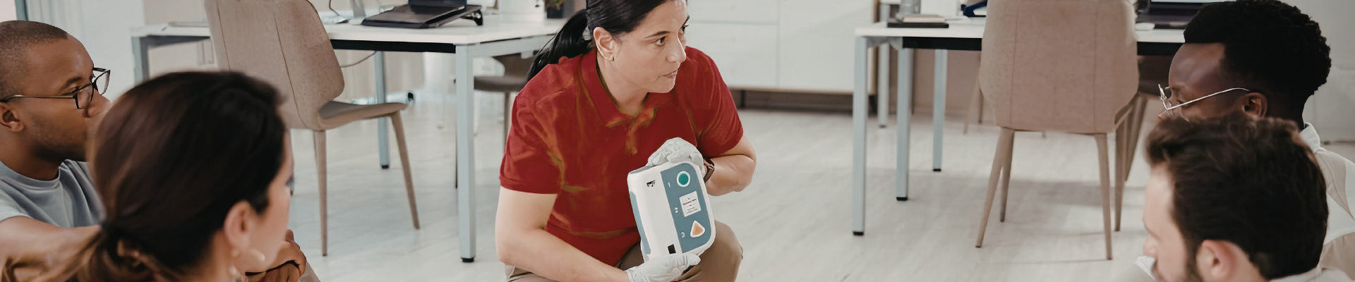 woman holding an automated external defibrillator and explaining how to use it to a group of people