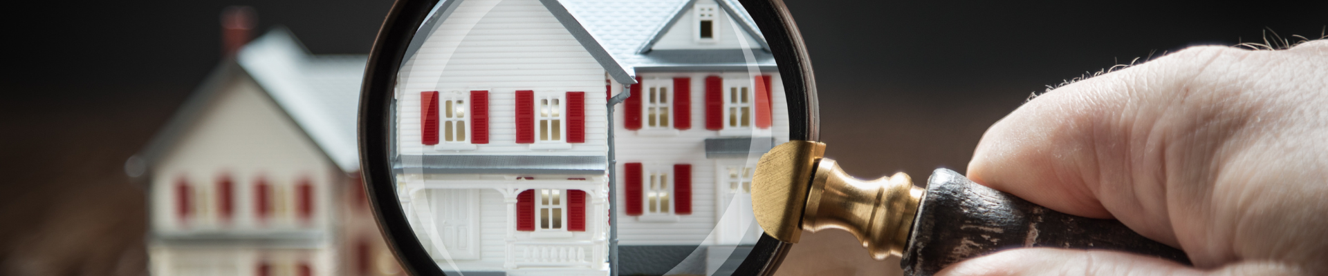 hand holding magnifying glass up to model house on wooden background