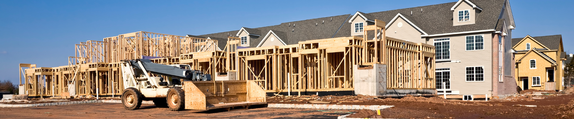 new homes under construction with machinery and road curb