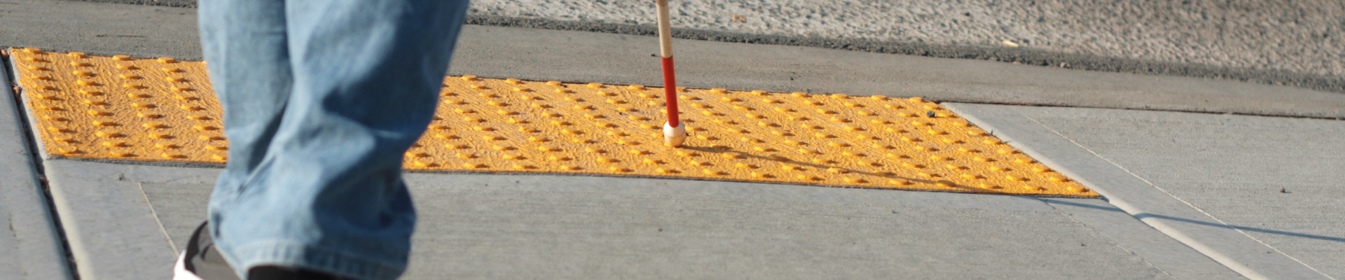 person using a cane crossing the street at a textured curb cut