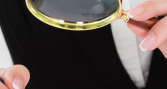 photo of two hands: one holding a pen, the other holding a magnifying glass