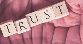 small blocks spelling TRUST, laid out in a person's two open hands