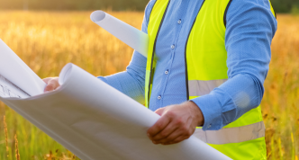 Photo of open land and person holding blueprint for construction