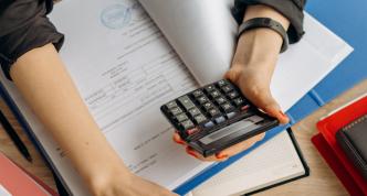 person holding open book and calculator at computer