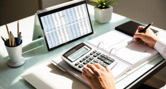Person calculating invoice costs using calculator, pencil, and computer screen