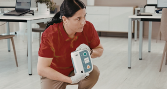 woman holding an automated external defibrillator and explaining how to use it to a group of people