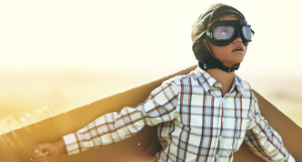 young boy pretending to fly with a pair of cardboard wings in an open field