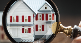 hand holding magnifying glass up to model house on wooden background