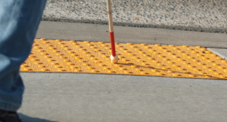person using a cane crossing the street at a textured curb cut